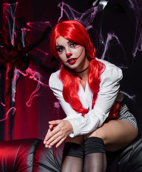 redhead woman in clown makeup looking at camera on dark background with spiderweb